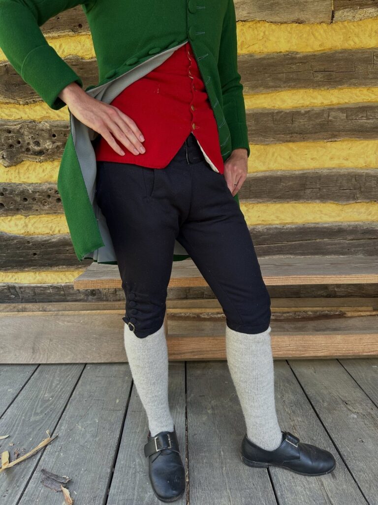 Man wearing dark knee-length breeches, white stockings, and black buckled shoes.