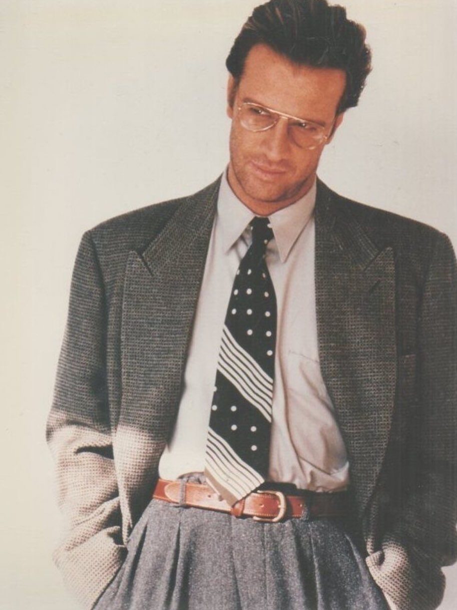 Man in 1980s business attire wearing a grey blazer, polka dot tie, and glasses.