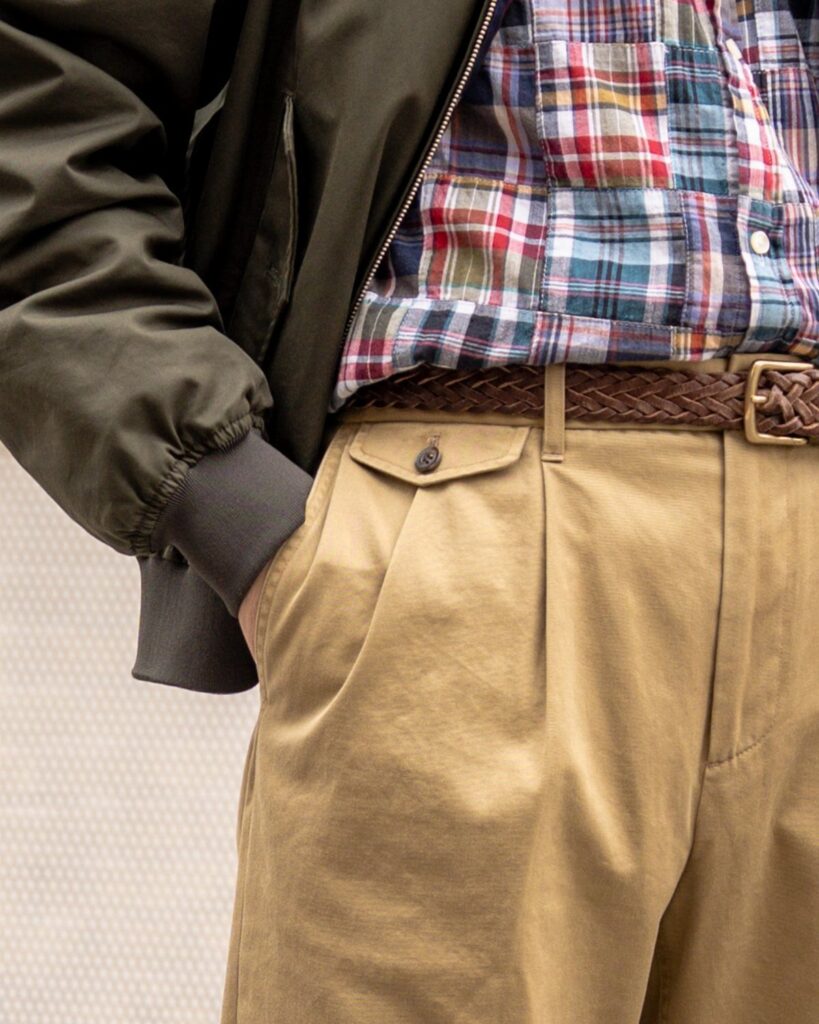 Man wearing a plaid shirt, khaki pleated pants, and olive green bomber jacket.