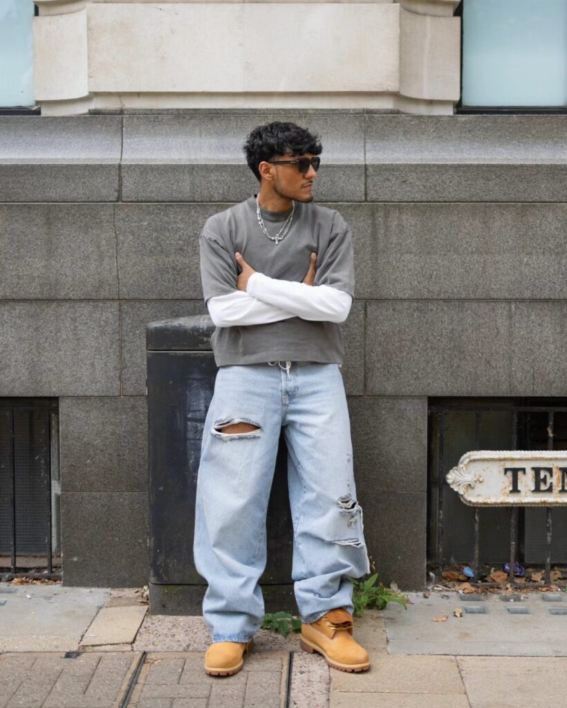 Man in oversized light-wash distressed baggy jeans and tan work boots posing outdoors.
