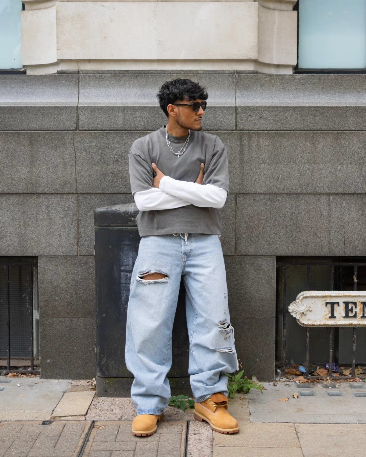 Man in oversized light-wash distressed baggy jeans and tan work boots posing outdoors.
