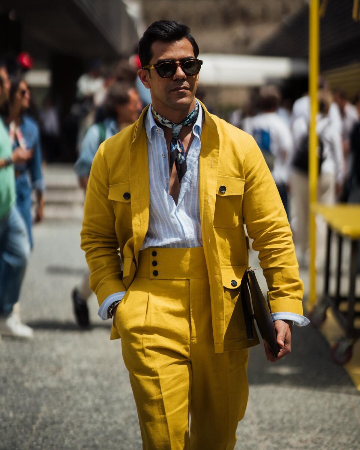 Man in a bright yellow suit with a white shirt and sunglasses walking outdoors.