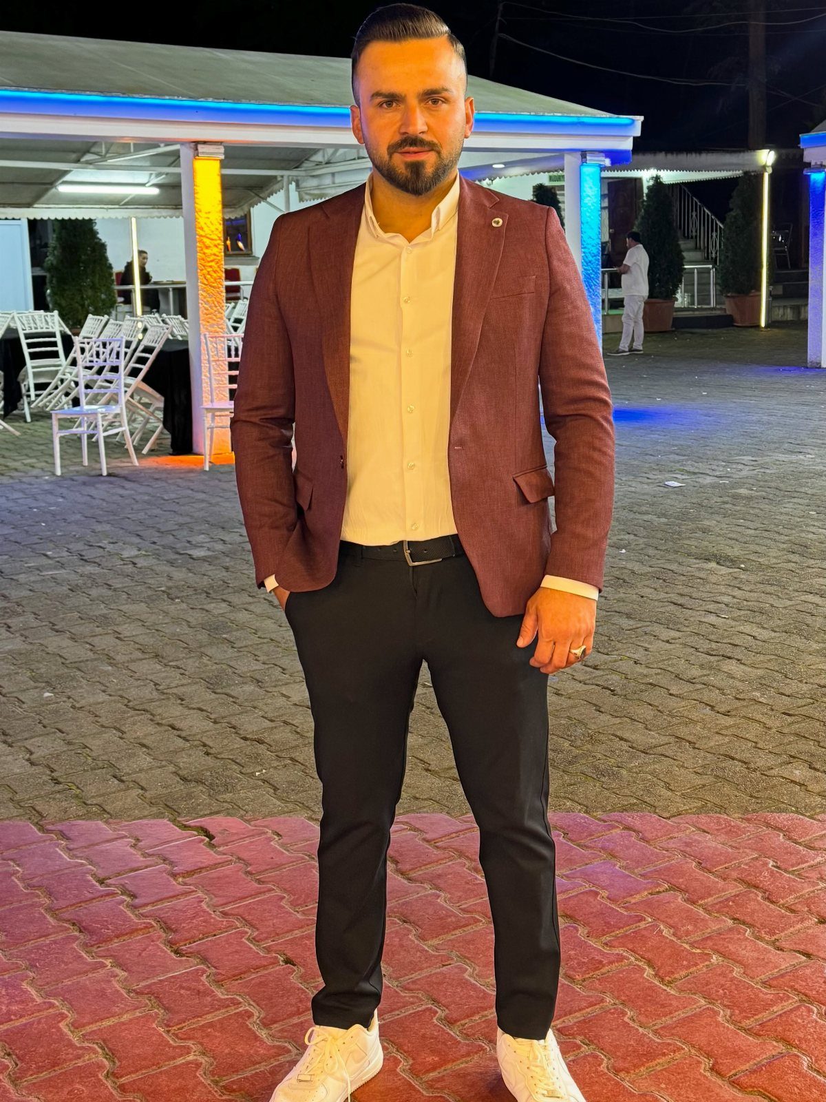 Man wearing a maroon blazer, white shirt, black pants, and white sneakers outdoors.