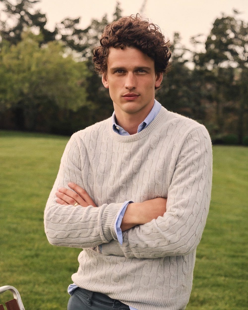Man wearing a grey cable-knit sweater and blue button-up shirt on a lawn