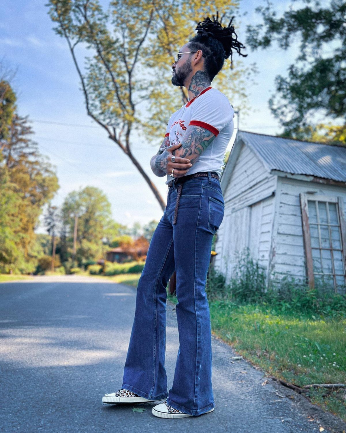 Man wearing high-waisted flare blue jeans and white t-shirt standing by a road.