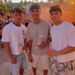 Three young men in casual summer t-shirts and shorts at an outdoor event.
