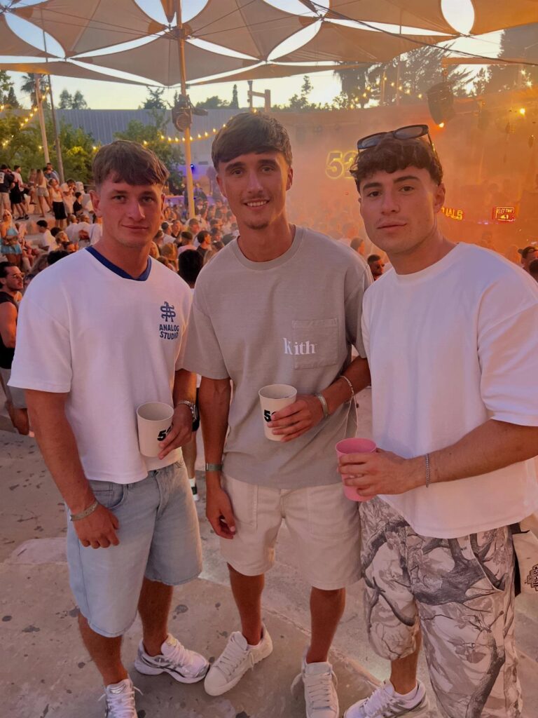 Three young men in casual summer t-shirts and shorts at an outdoor event.