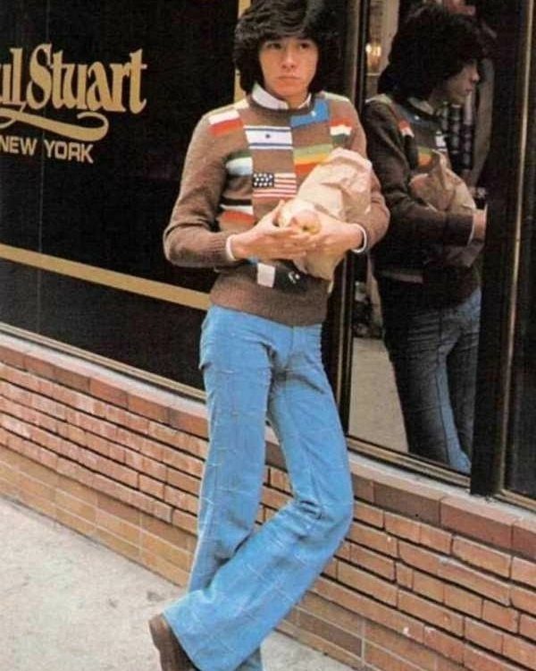 Man in 1970s fashion wearing a striped sweater and wide blue flared trousers.