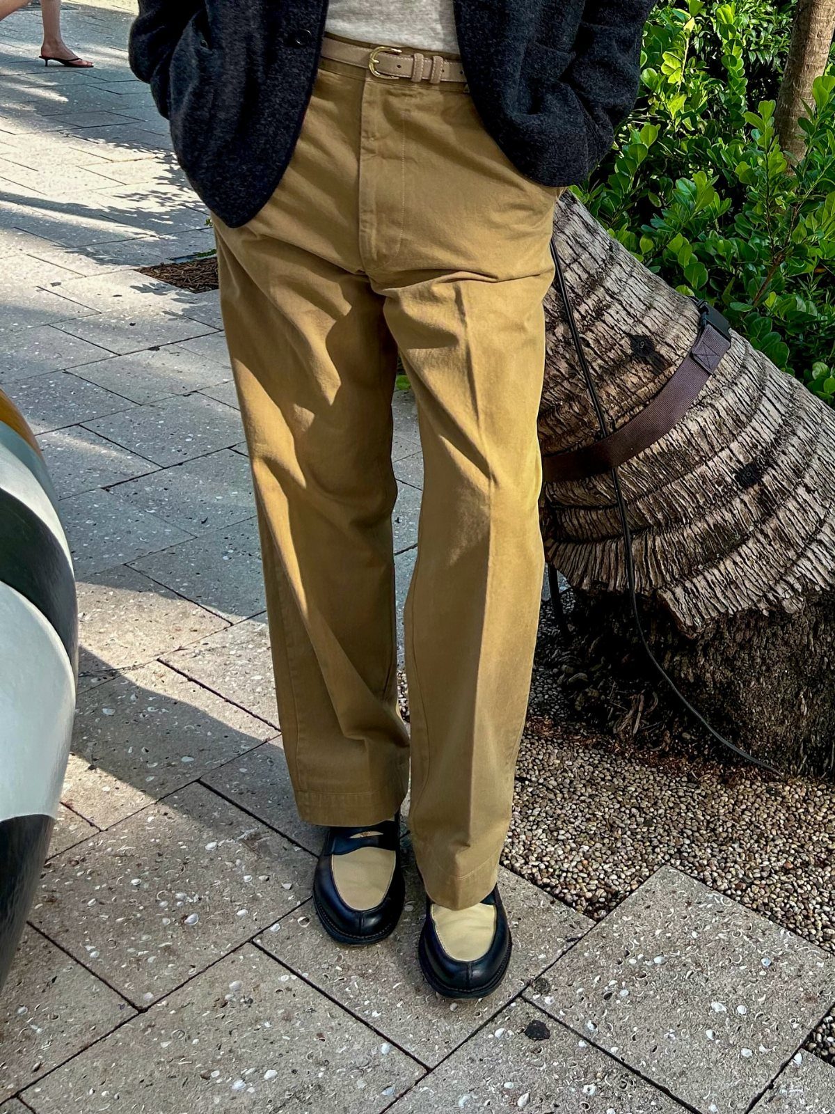 Person wearing high-waisted tan chinos, a dark cardigan, and black and beige loafers.
