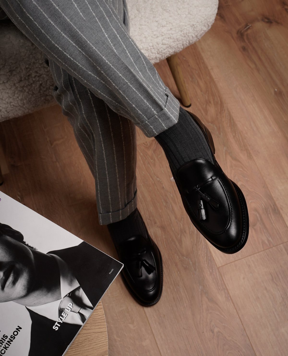 Black leather tassel loafers worn with grey pinstriped trousers and black socks.