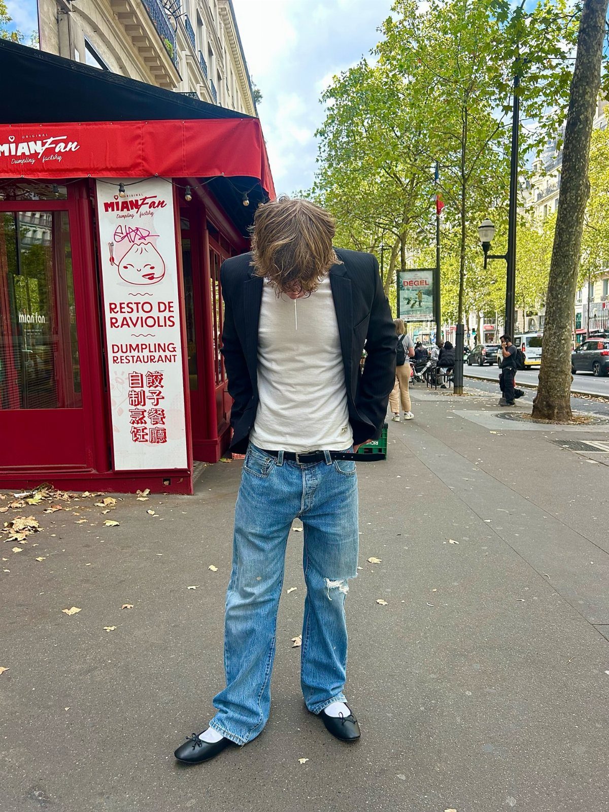 Man wearing black ballet flats, blue jeans, and a blazer on a city street