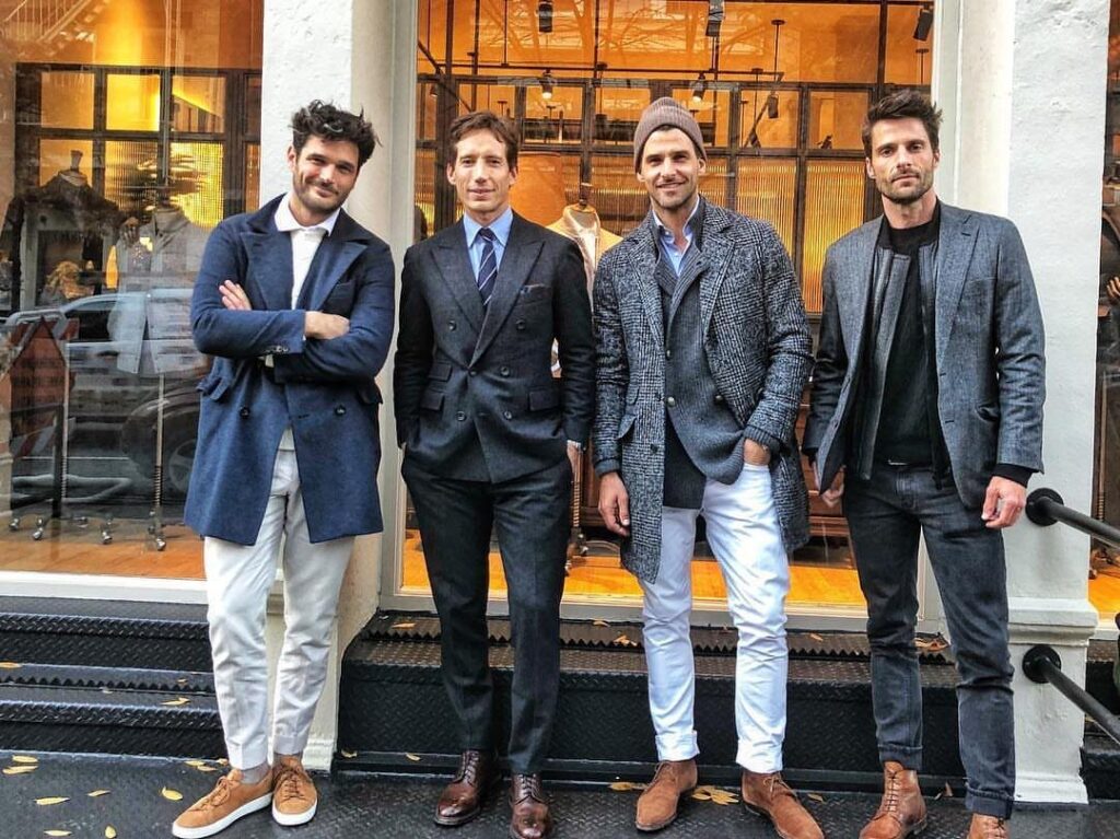 Four men in stylish blazers and coats posing outside a Soho clothing store.