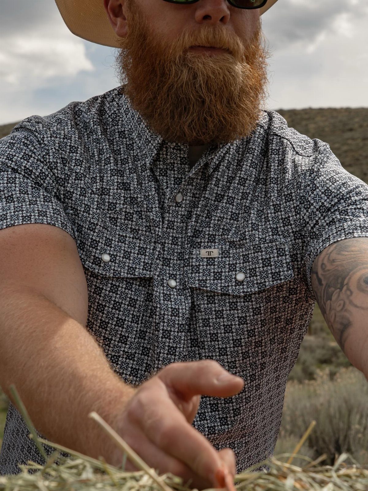 Man with red beard wearing a patterned pearl snap western shirt and cowboy hat.