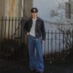 Man in a simple outfit with a grey jacket and wide blue jeans.