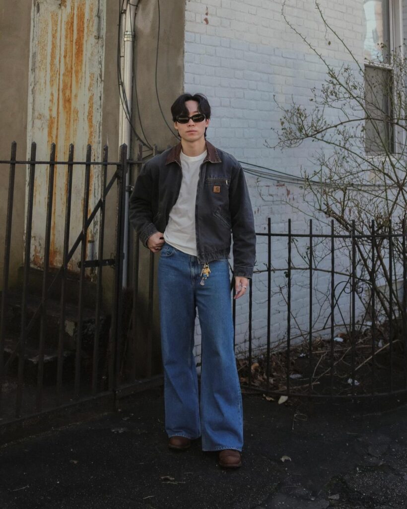 Man in a simple outfit with a grey jacket and wide blue jeans.