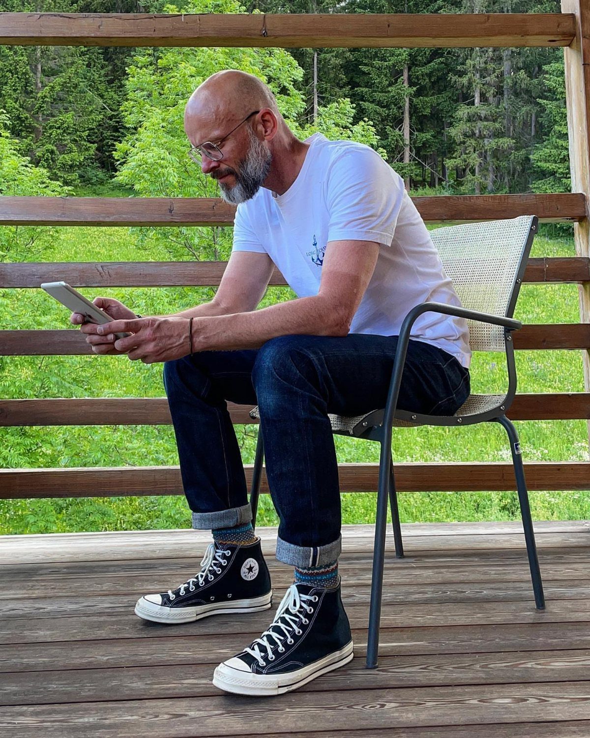 Man in white t-shirt and cuffed jeans wearing black high-top Converse sneakers.