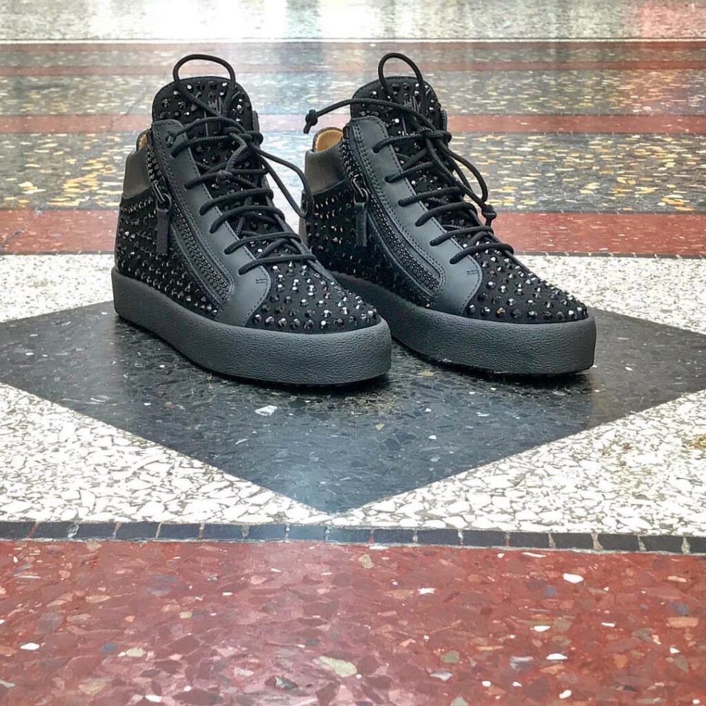 Black high-top sneakers with silver studs and zippers on a terrazzo floor