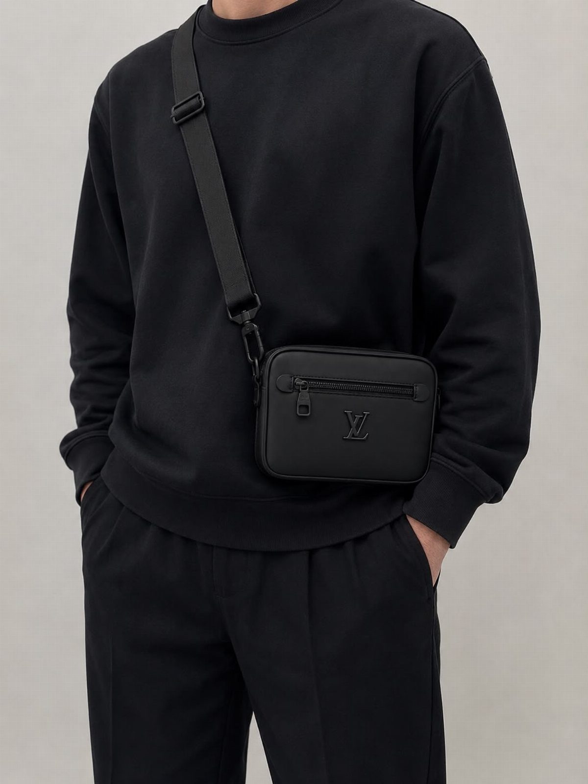 Man wearing a black crossbody fashion purse over a black sweatshirt and trousers.
