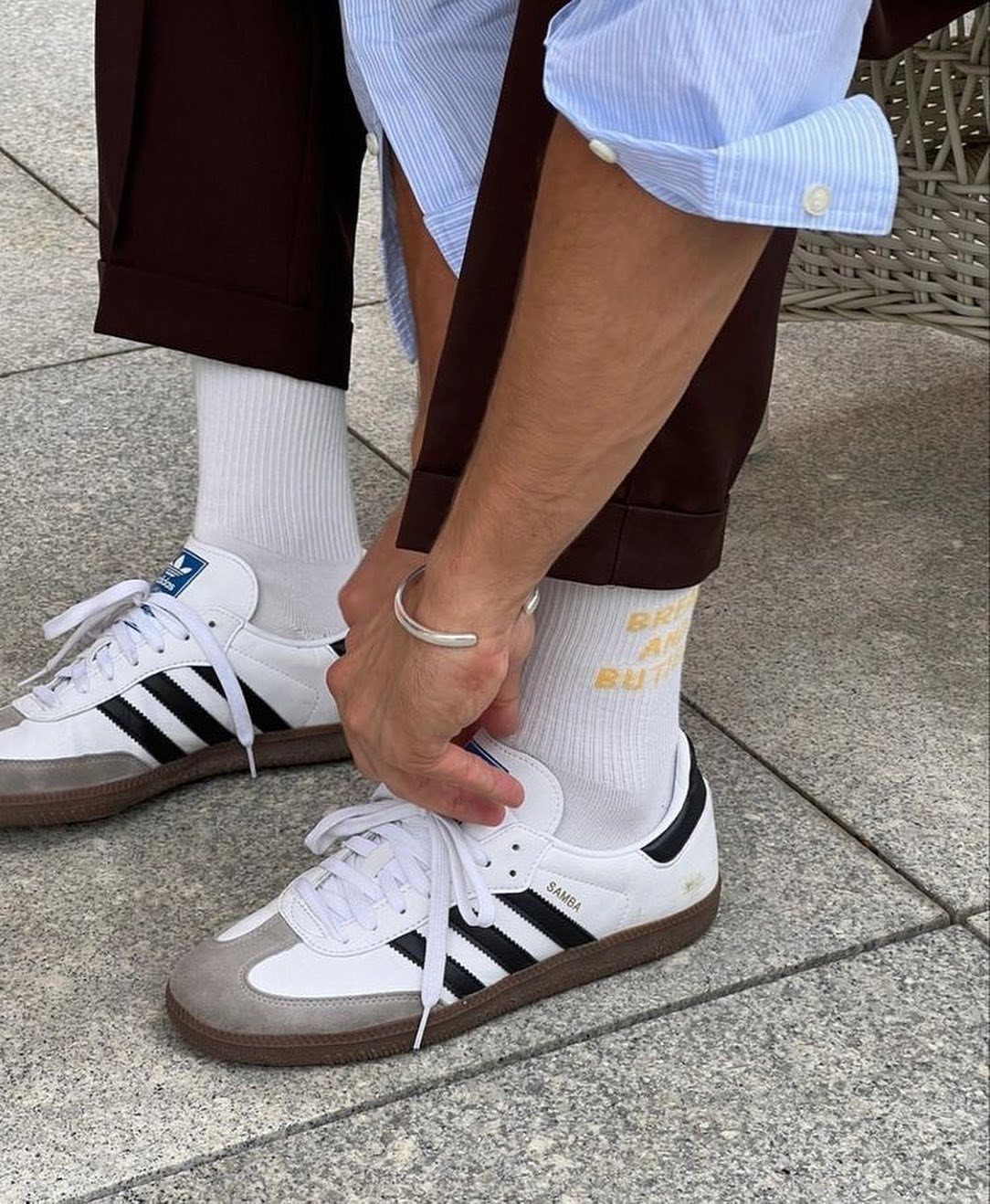 White adidas Samba sneakers with black stripes and brown soles on a person.