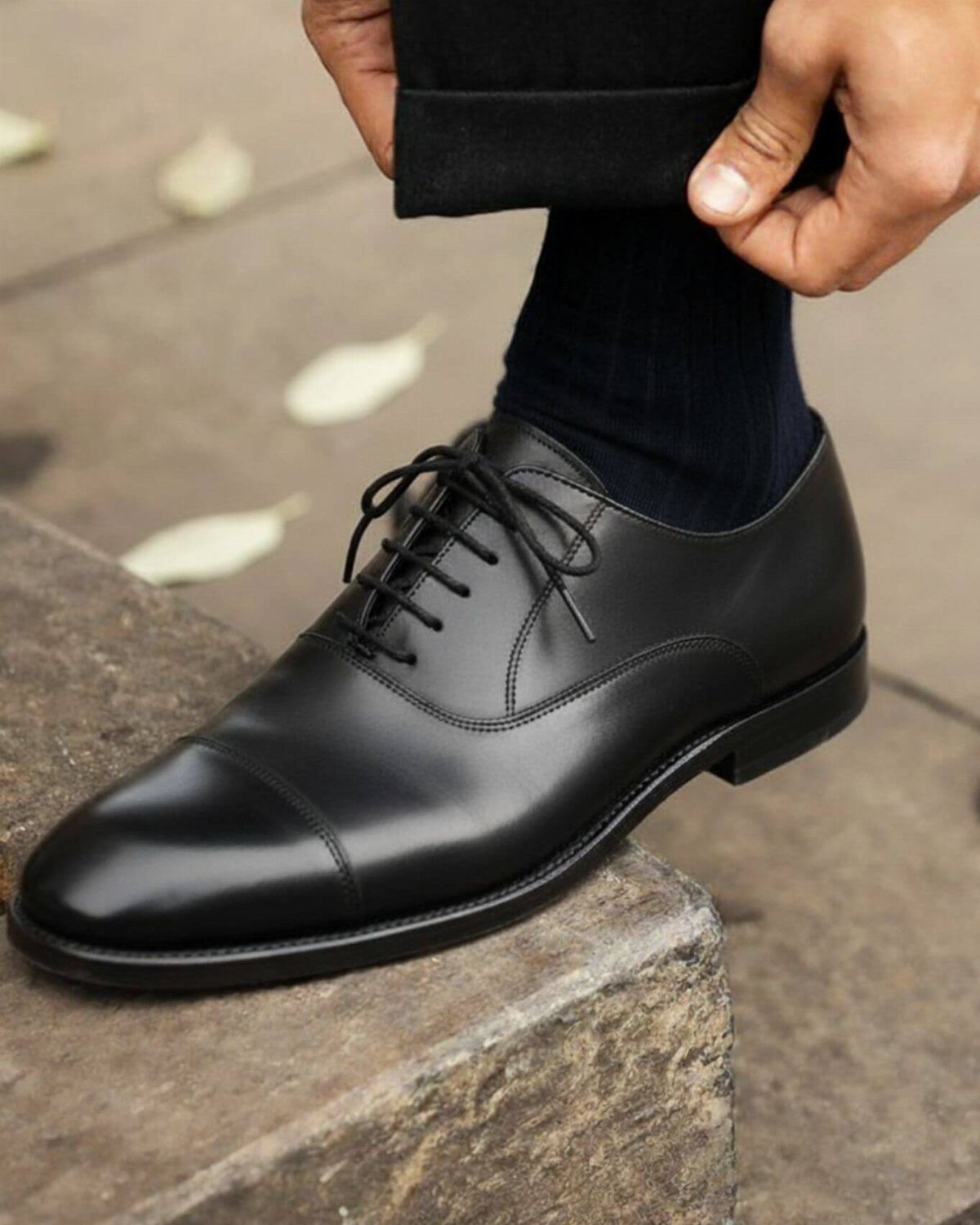 Black leather cap-toe oxford shoe on a foot resting on a stone step
