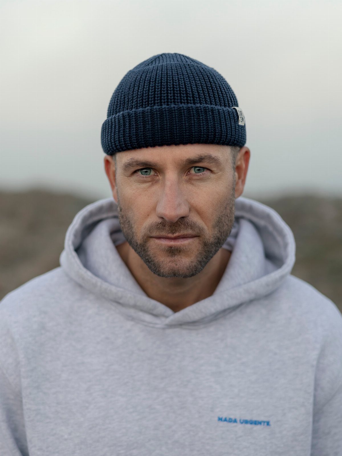 Man wearing a dark blue ribbed knit beanie and a grey hoodie.