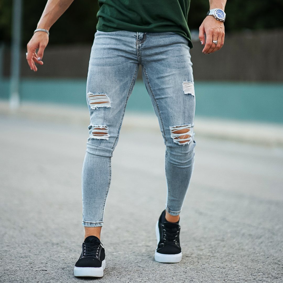 Man wearing light blue distressed skinny jeans and black sneakers on a road.