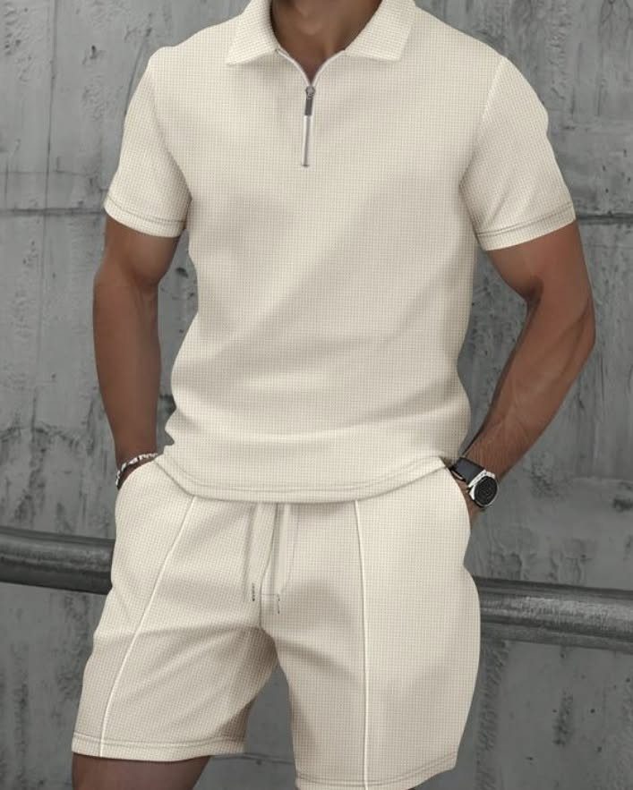 Man wearing a cream quarter-zip polo shirt and matching shorts against a concrete wall.