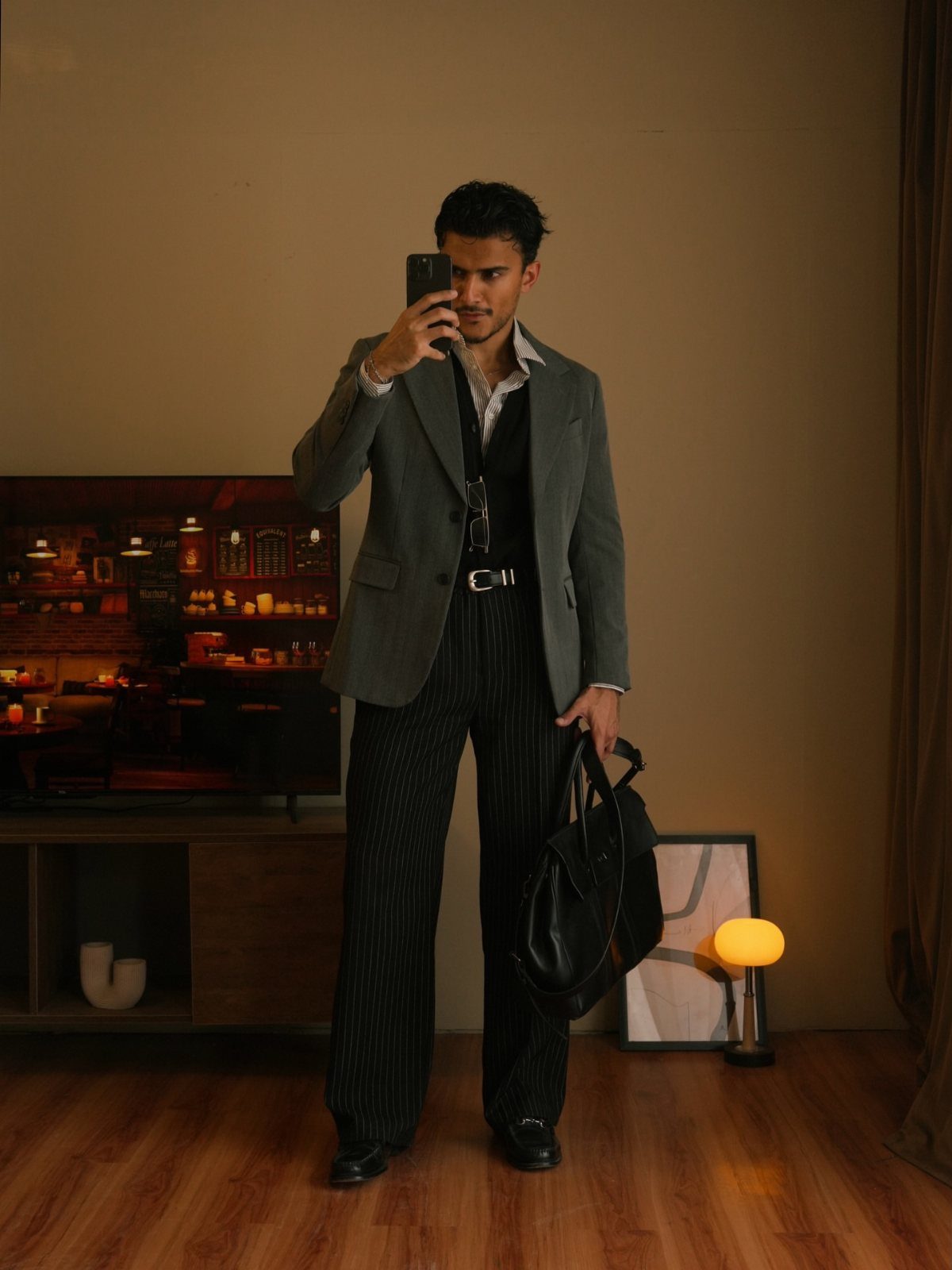Man in a grey blazer and pinstriped trousers taking a mirror selfie indoors.