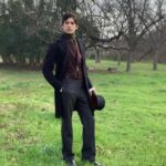 Man in Victorian era clothing including a frock coat and top hat in a field.