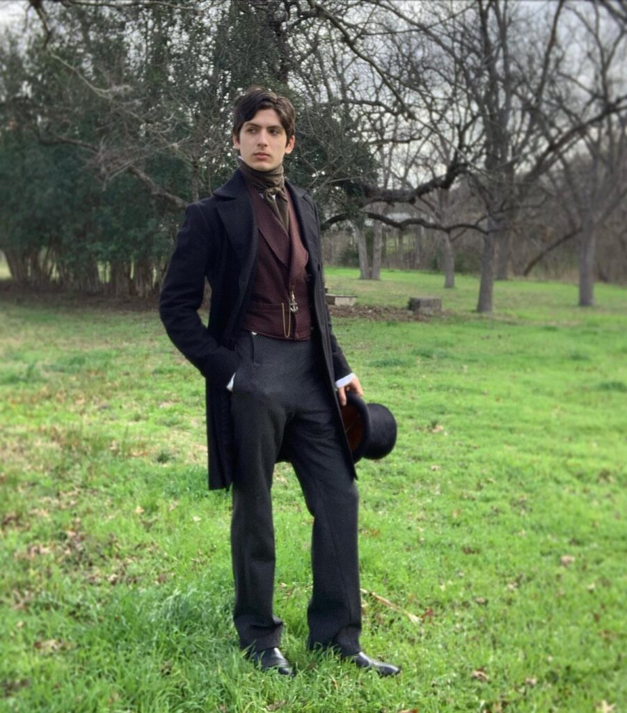 Man in Victorian era clothing including a frock coat and top hat in a field.
