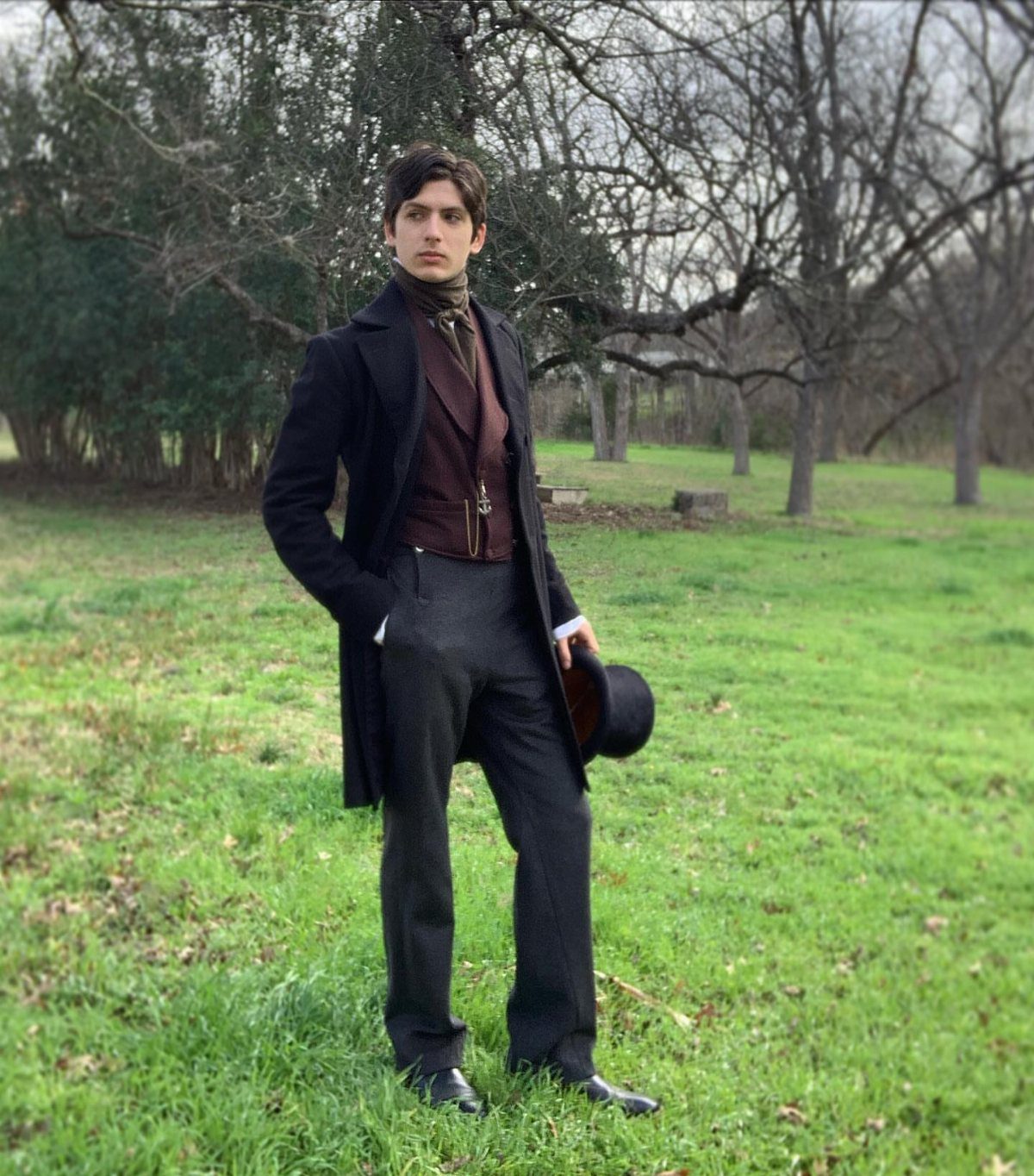 Man in Victorian era clothing including a frock coat and top hat in a field.