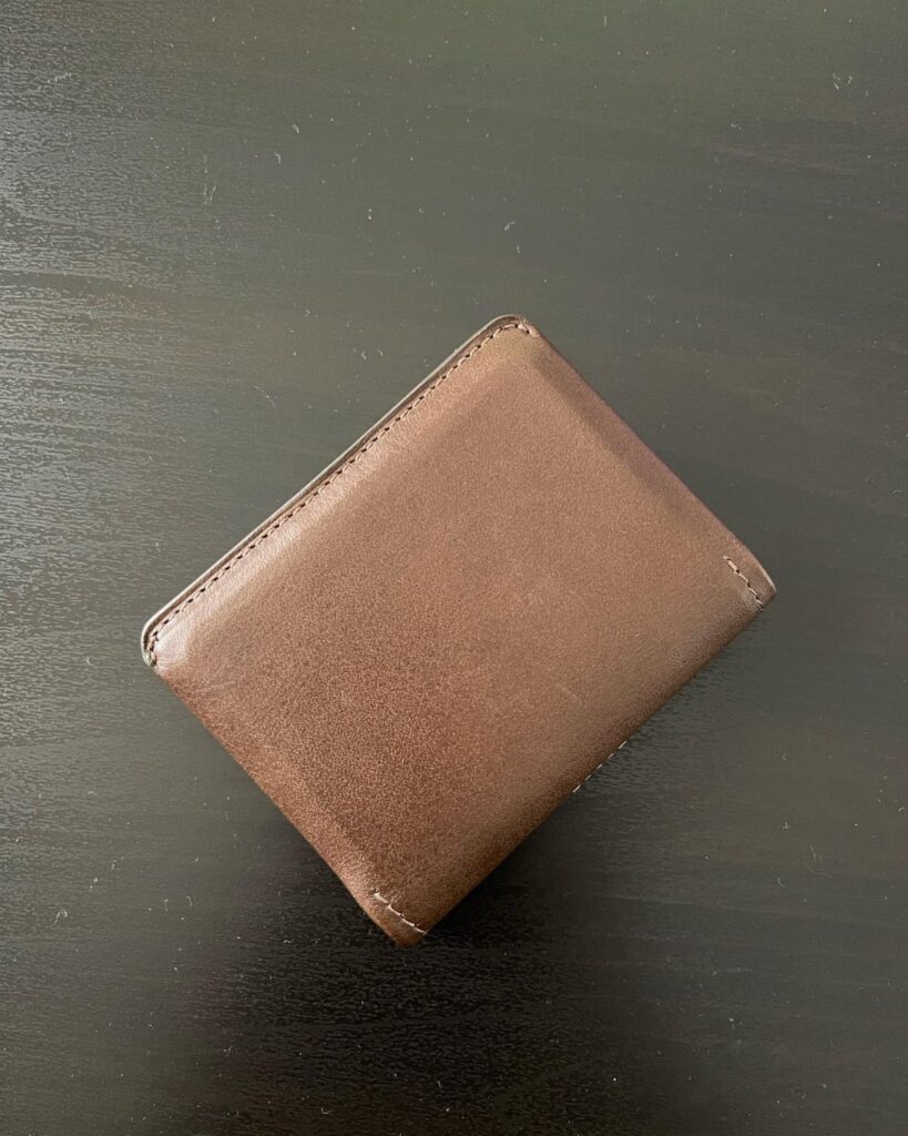 Brown leather bifold wallet resting on a dark black tabletop surface.