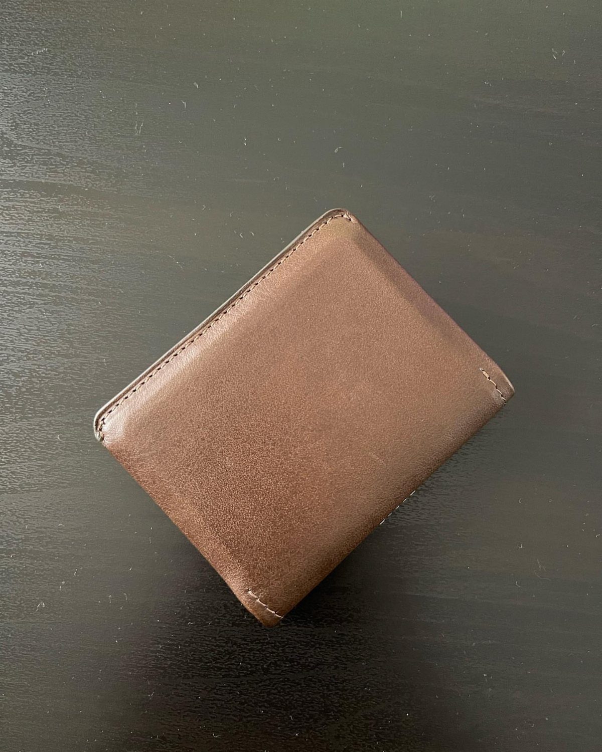 Brown leather bifold wallet resting on a dark black tabletop surface.