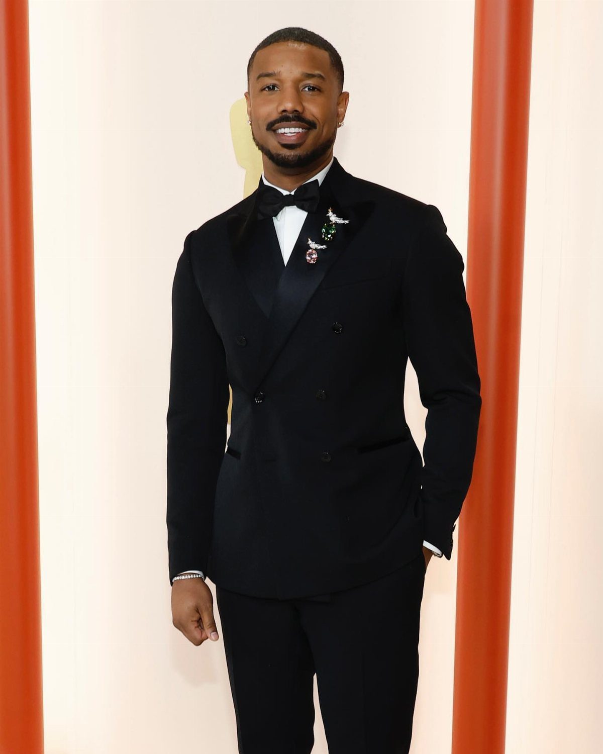 Man in a black double-breasted tuxedo and bow tie posing for a photo.