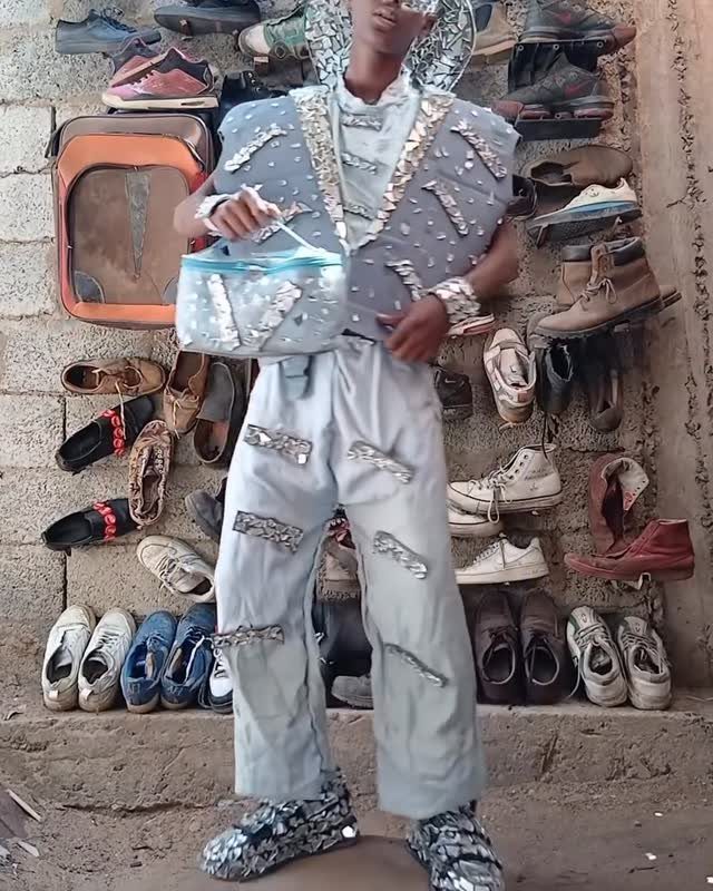 Man in an embellished light blue suit and handbag posing before a shoe wall.